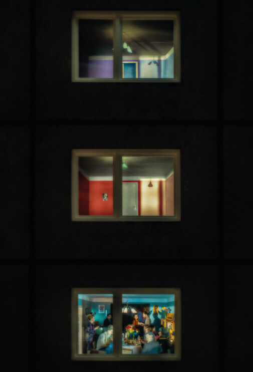 Night time scene of an apartment building from the outside, looking in the windows. By Joelle Chmiel