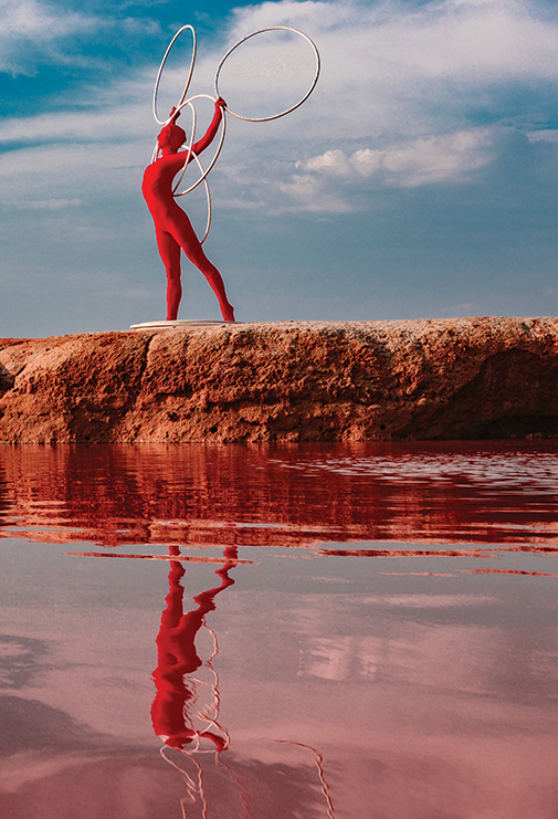 a figure in a red bodysuit stands on a red dusty edge of the water, holding four white rings above their head.